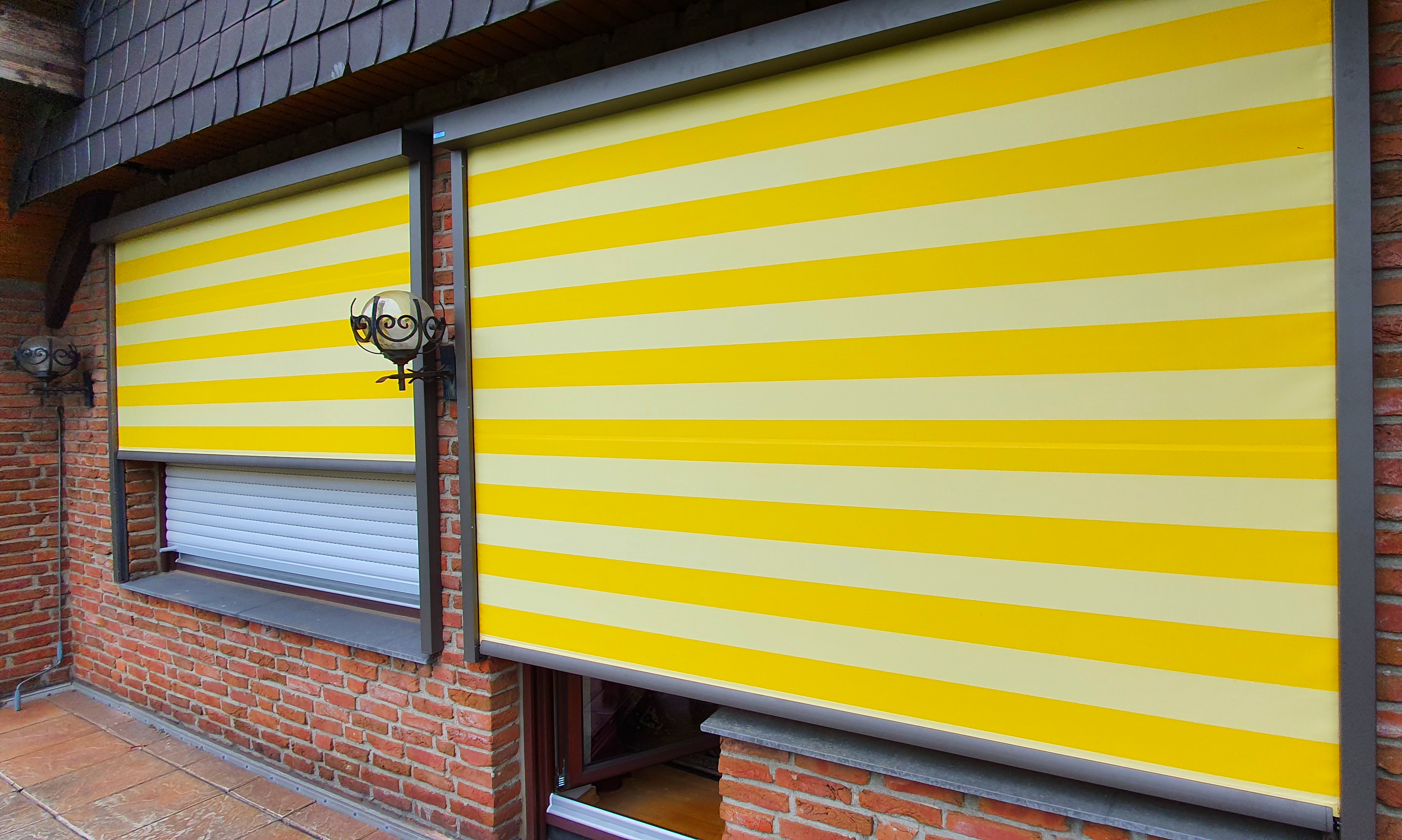 Zwei Vertikalmarkisen in gelb an einem Klinkerhaus