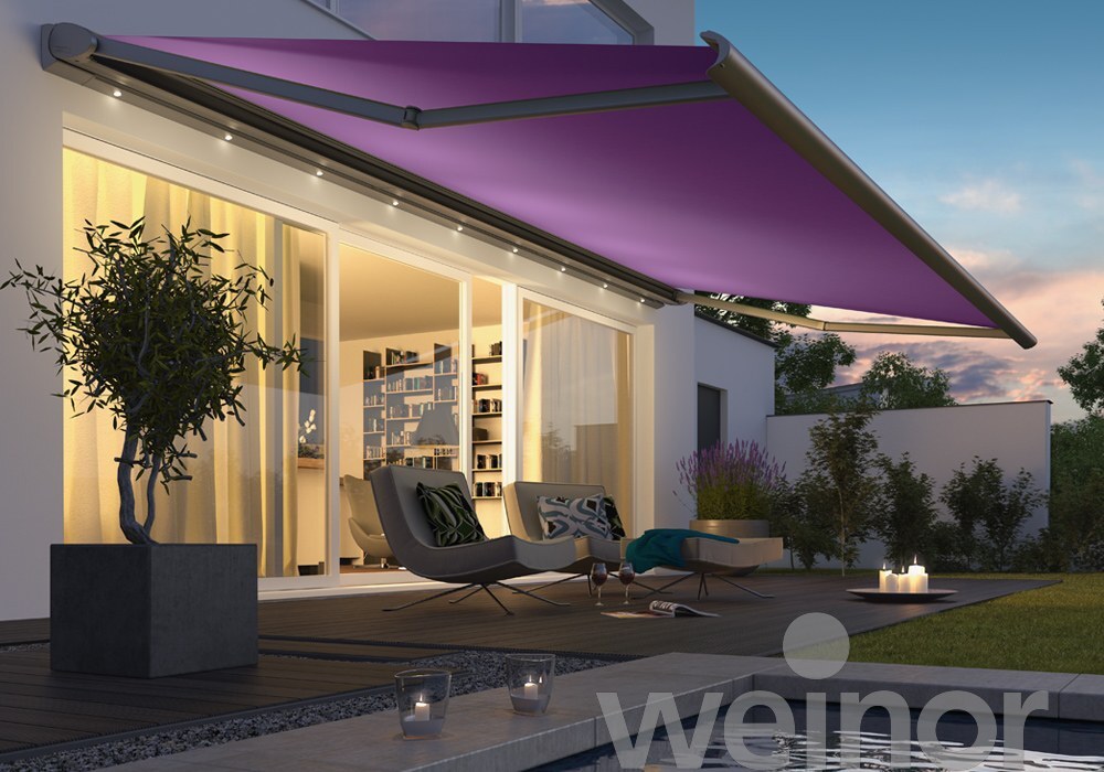 Geöffnete Markise mit lila Tuch und LED-Leiste während der Dämmerung. Vor der Terrasse ist ein Pool und die Schiebetür ins Haus ist geöffnet.