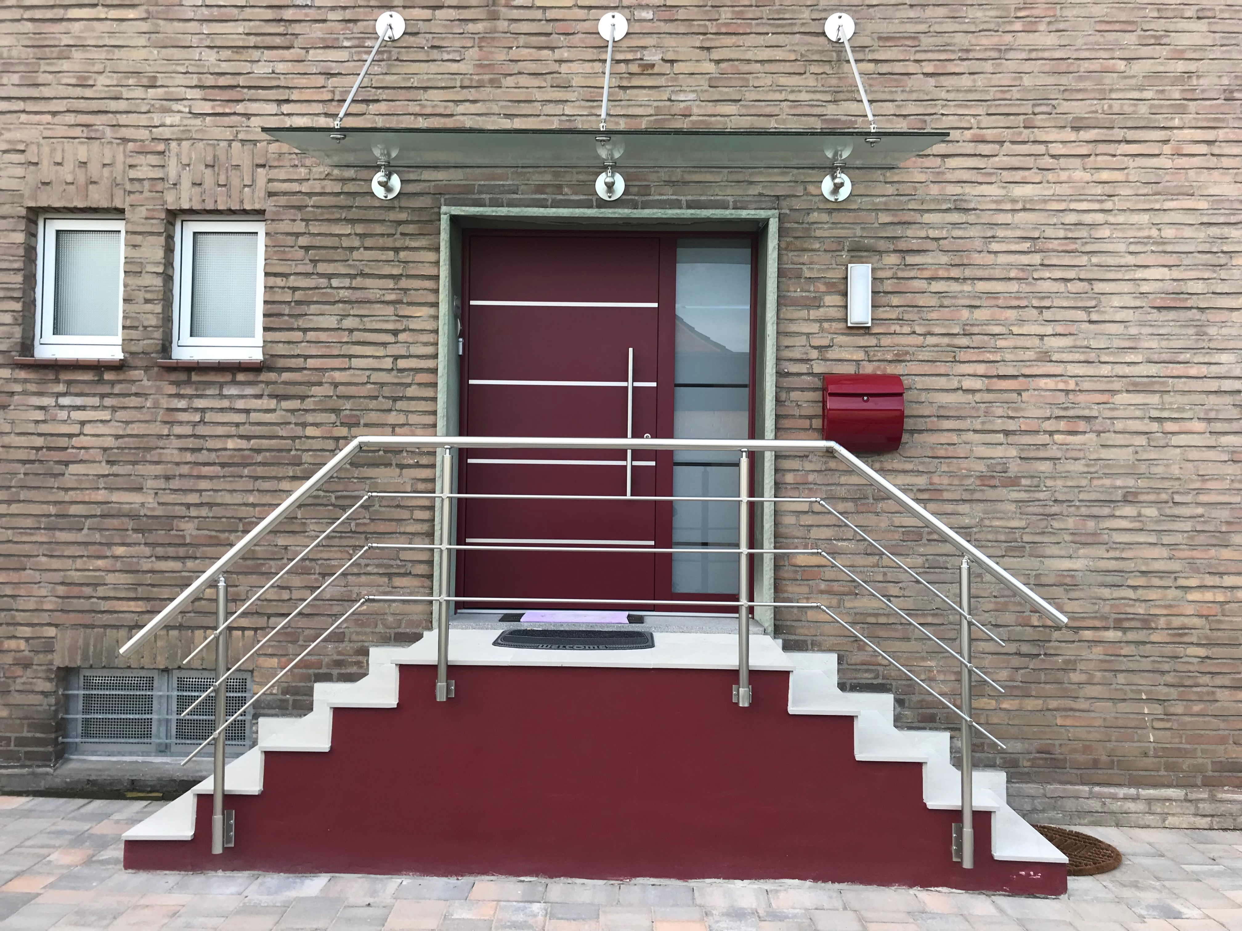 Rote Aluminium Haustür in Übergröße unter einem Glasvordach