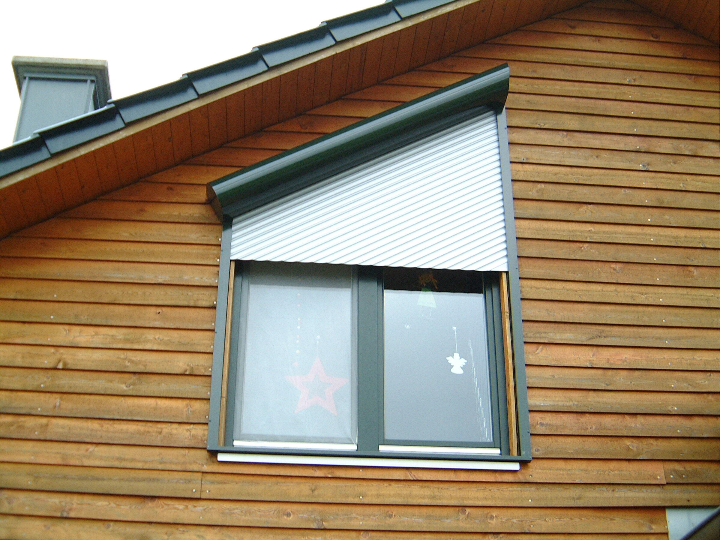 Schräger Vorbaurollladen in Grün an einem Holzhaus